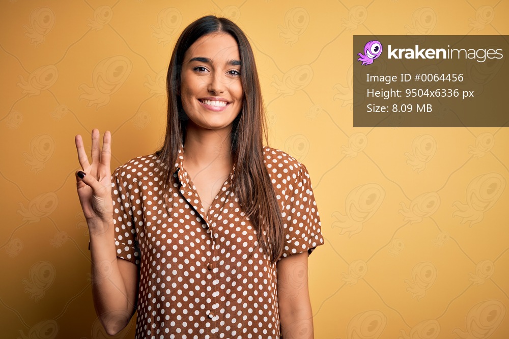 Young beautiful brunette woman wearing casual shirt over isolated yellow background showing and pointing up with fingers number three while smiling confident and happy.