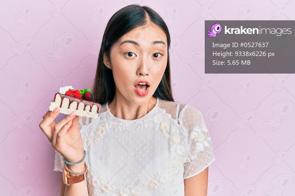 Young chinese woman eating a tasty cake scared and amazed with open mouth for surprise, disbelief face 