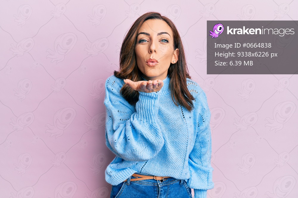 Young brunette woman wearing casual winter sweater over pink background looking at the camera blowing a kiss with hand on air being lovely and sexy. love expression. 