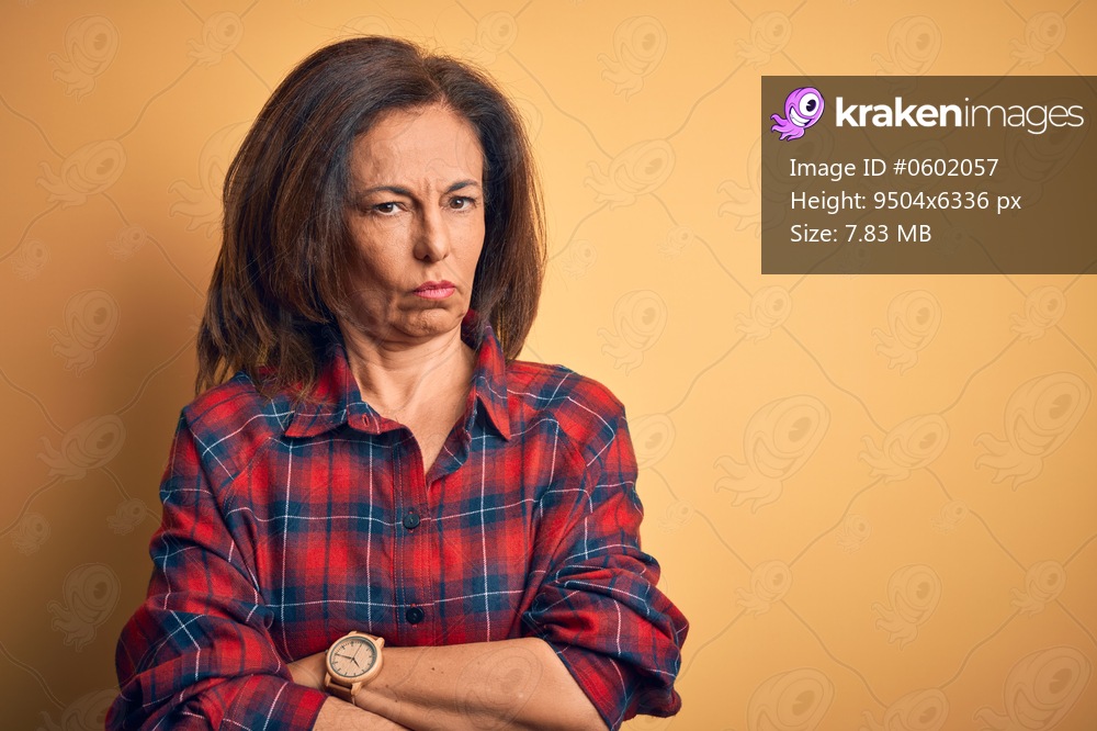 Middle age beautiful woman wearing casual shirt standing over isolated yellow background skeptic and nervous, disapproving expression on face with crossed arms. Negative person.