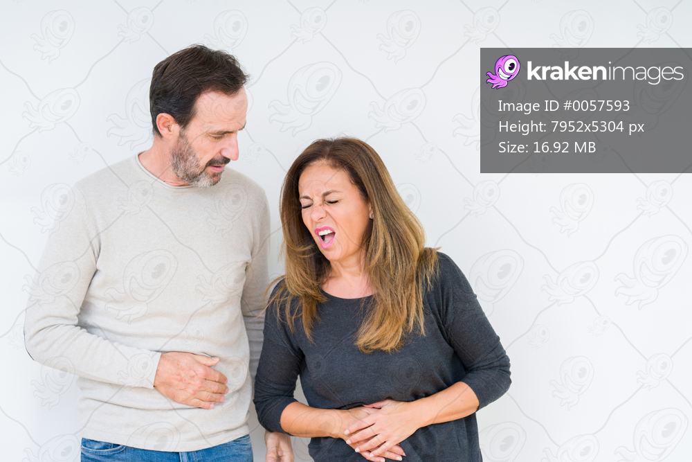 Beautiful middle age couple in love over isolated background with hand on stomach because indigestion, painful illness feeling unwell. Ache concept.