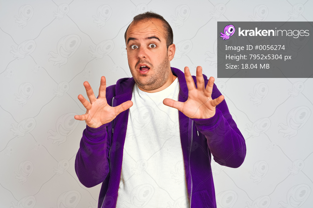 Young man wearing purple sweatshirt standing over isolated white background afraid and terrified with fear expression stop gesture with hands, shouting in shock. Panic concept.