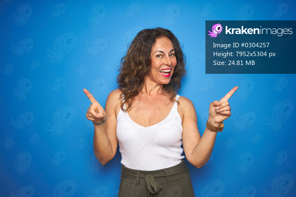 Middle age senior woman with curly hair standing over blue isolated background smiling confident pointing with fingers to different directions. Copy space for advertisement