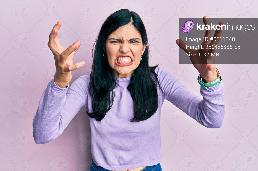 Young hispanic woman wearing casual clothes shouting frustrated with rage, hands trying to strangle, yelling mad 