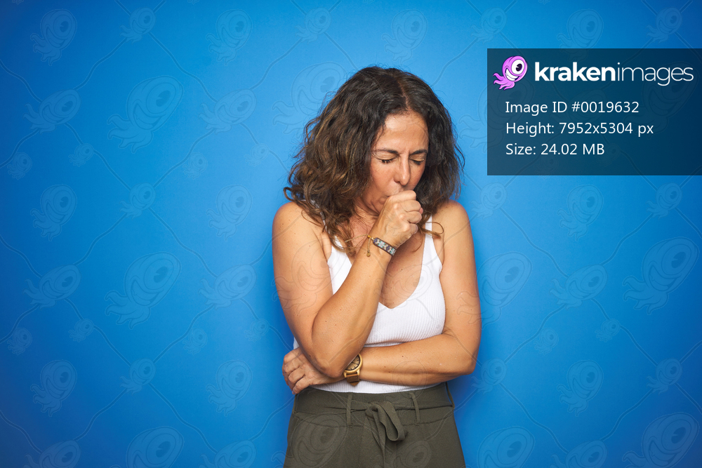 Middle age senior woman with curly hair standing over blue isolated background feeling unwell and coughing as symptom for cold or bronchitis. Healthcare concept.