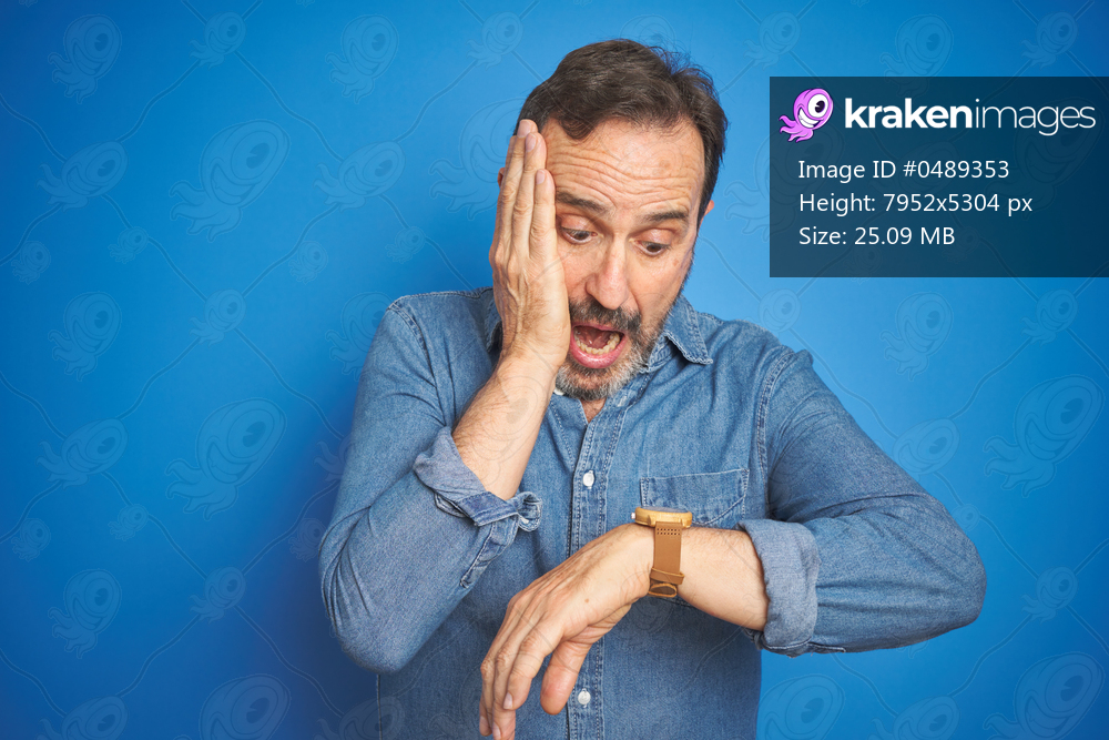 Handsome middle age senior man with grey hair over isolated blue background Looking at the watch time worried, afraid of getting late