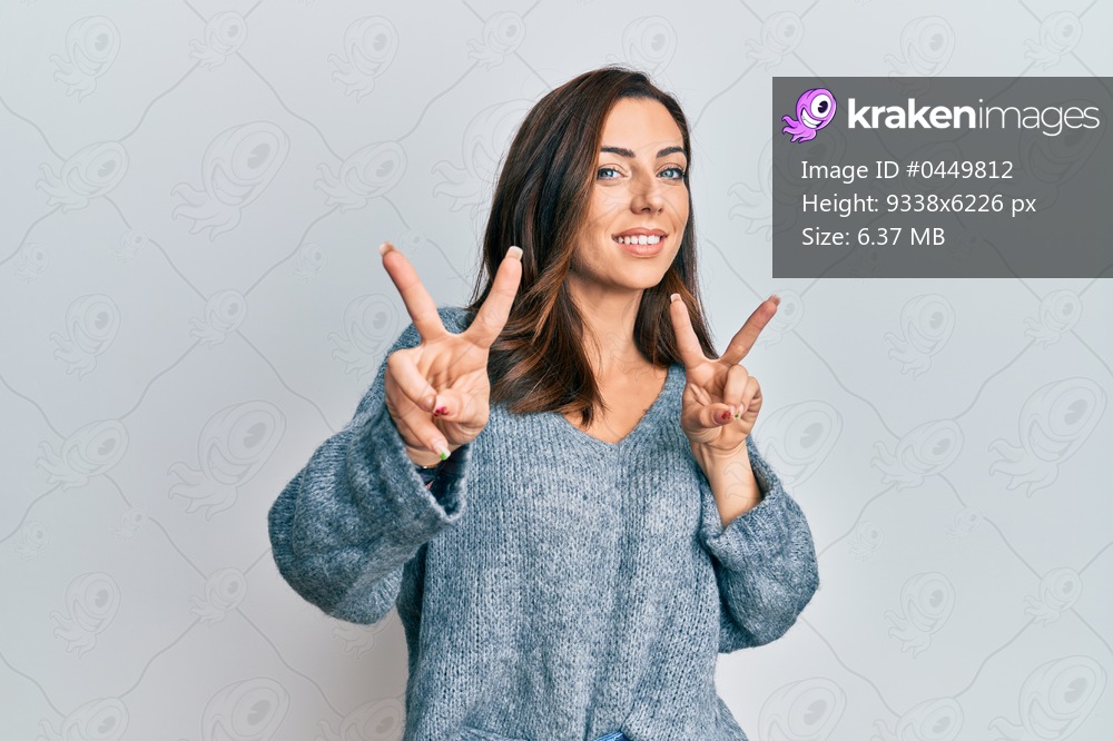 Young brunette woman wearing casual winter sweater smiling looking to the camera showing fingers doing victory sign. number two. 