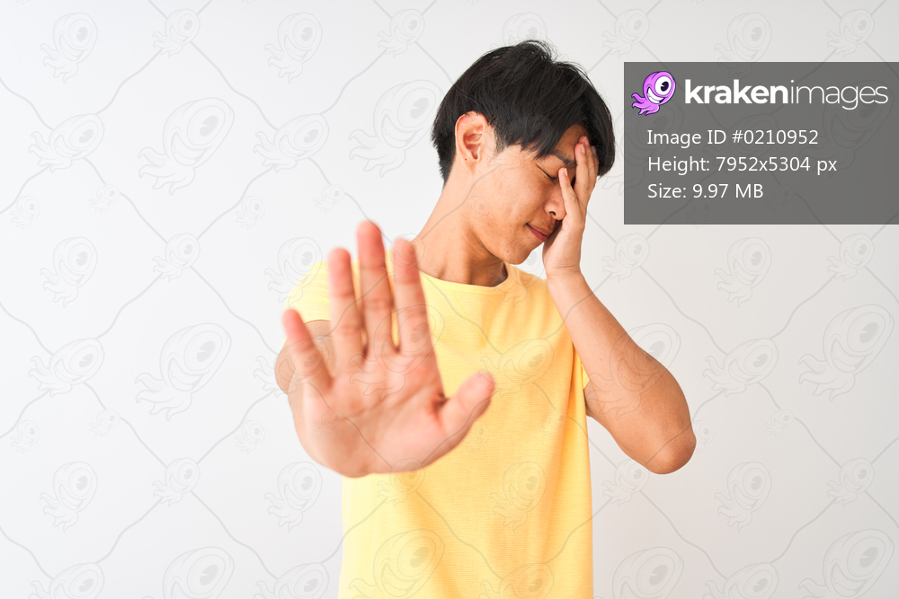 Chinese man wearing yellow casual t-shirt standing over isolated white background covering eyes with hands and doing stop gesture with sad and fear expression. Embarrassed and negative concept.