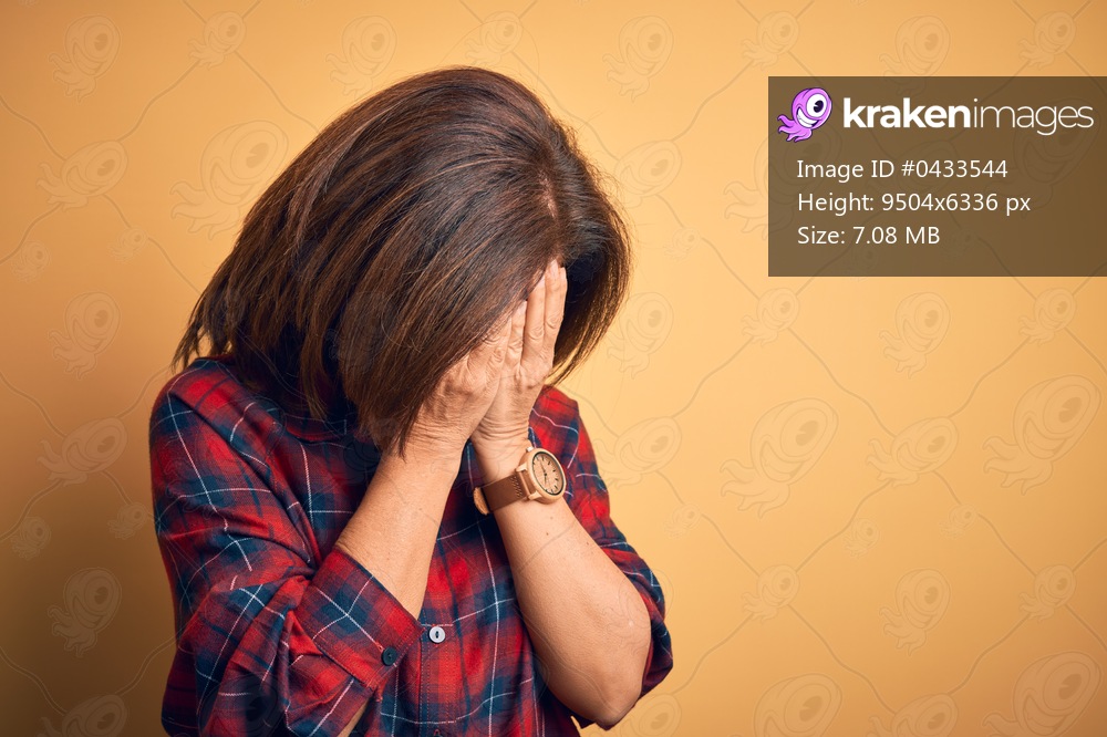Middle age beautiful woman wearing casual shirt standing over isolated yellow background with sad expression covering face with hands while crying. Depression concept.