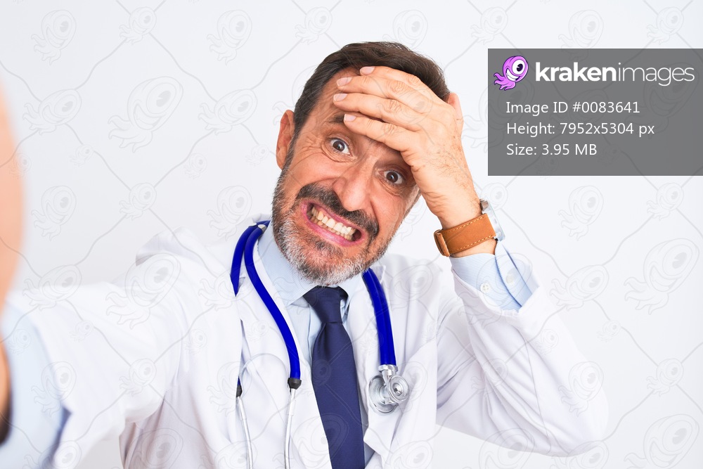 Middle age doctor man wearing stethoscope make selfie over isolated white background stressed with hand on head, shocked with shame and surprise face, angry and frustrated. Fear and upset for mistake.