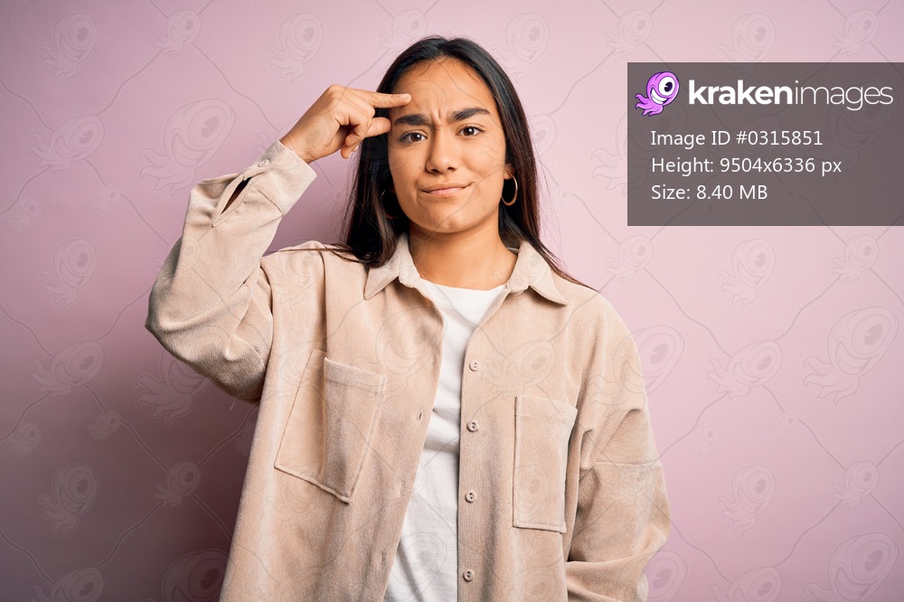 Young beautiful asian woman wearing casual shirt standing over pink background pointing unhappy to pimple on forehead, ugly infection of blackhead. Acne and skin problem