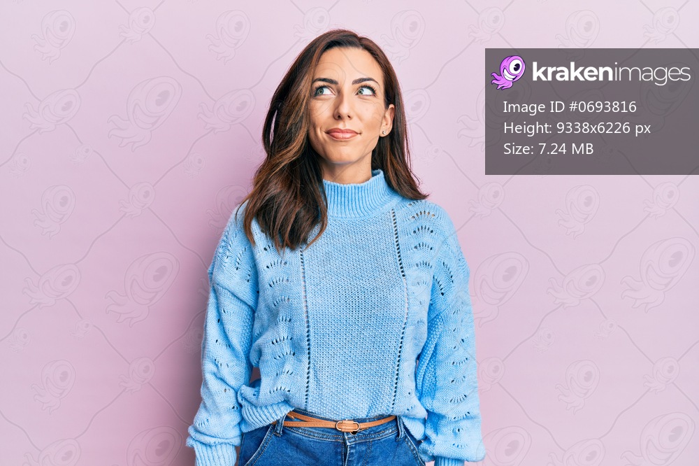 Young brunette woman wearing casual winter sweater over pink background smiling looking to the side and staring away thinking. 