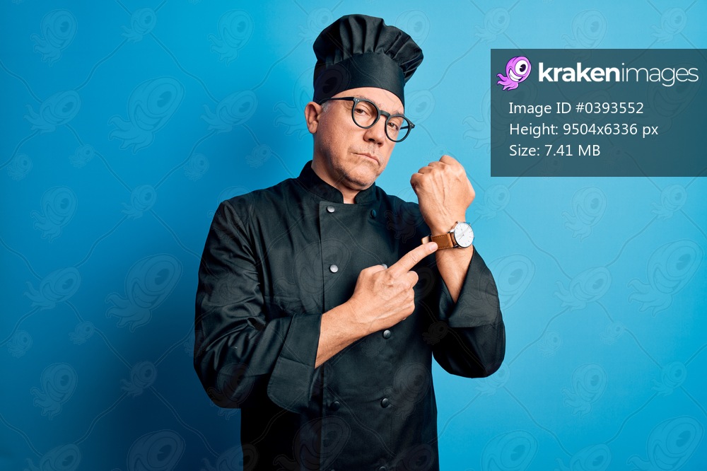 Middle age handsome grey-haired chef man wearing cooker uniform and hat In hurry pointing to watch time, impatience, looking at the camera with relaxed expression