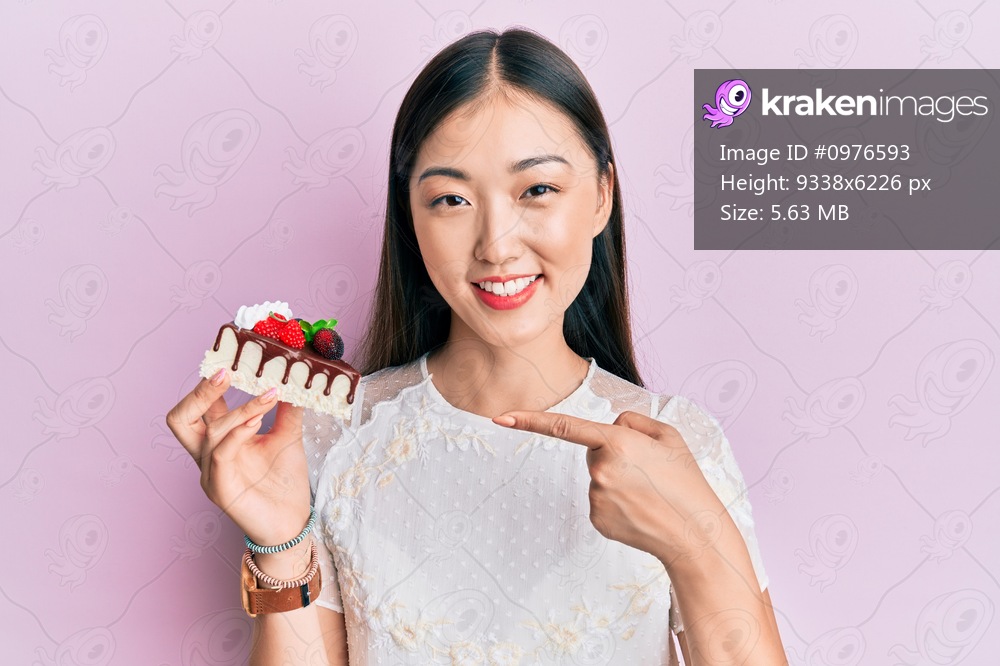 Young chinese woman eating a tasty cake smiling happy pointing with hand and finger 