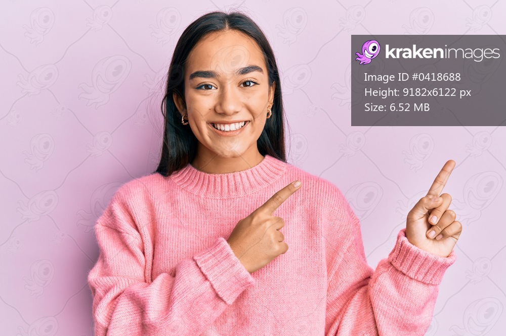 Young asian woman wearing casual winter sweater smiling and looking at the camera pointing with two hands and fingers to the side. 