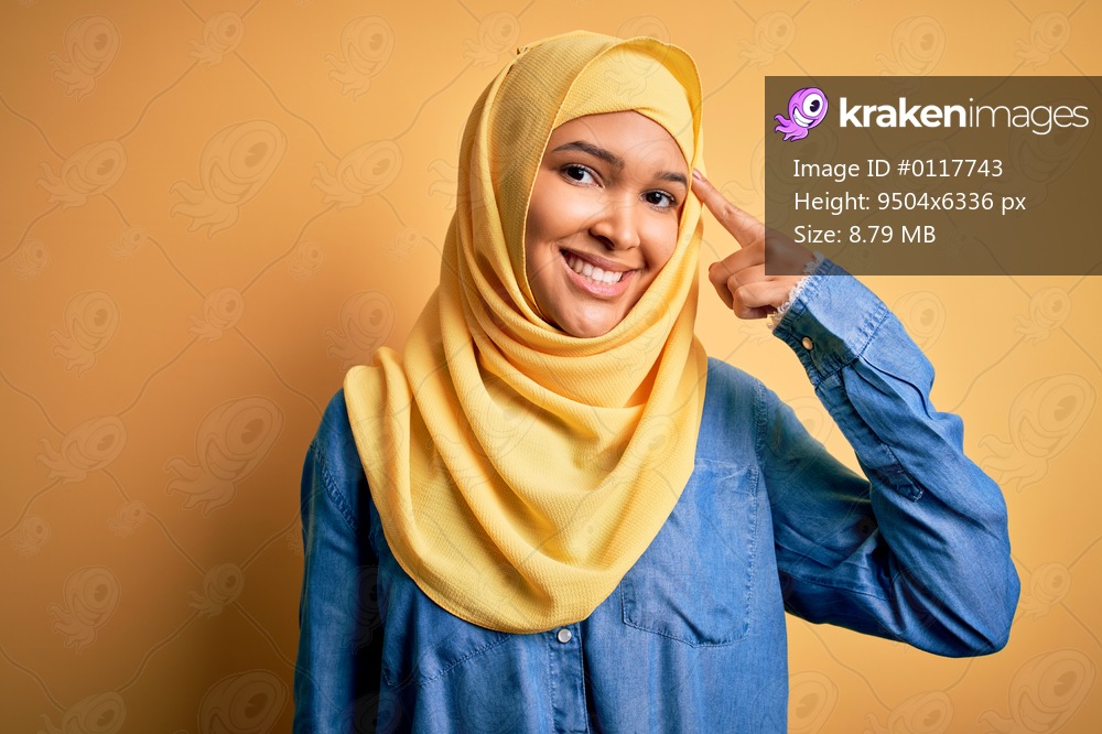 Young beautiful woman with curly hair wearing arab traditional hijab over yellow background Smiling pointing to head with one finger, great idea or thought, good memory