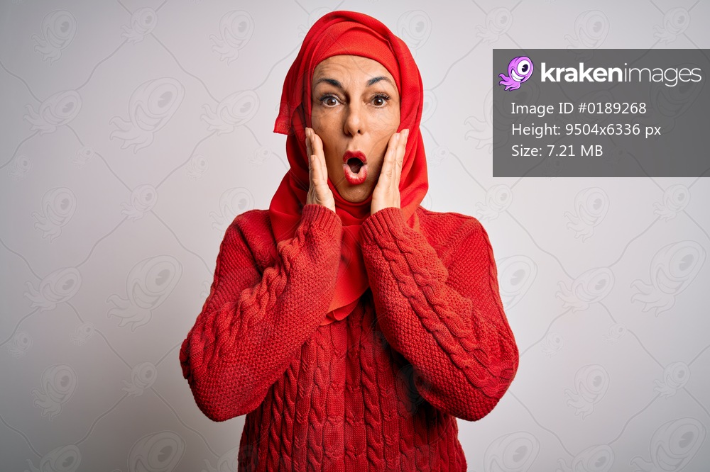 Middle age brunette woman wearing muslim traditional hijab over isolated white background afraid and shocked, surprise and amazed expression with hands on face