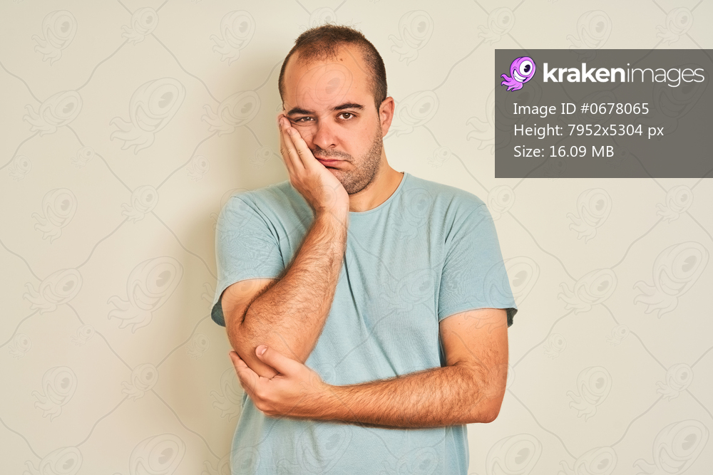 Young man wearing blue casual t-shirt standing over isolated white background thinking looking tired and bored with depression problems with crossed arms.