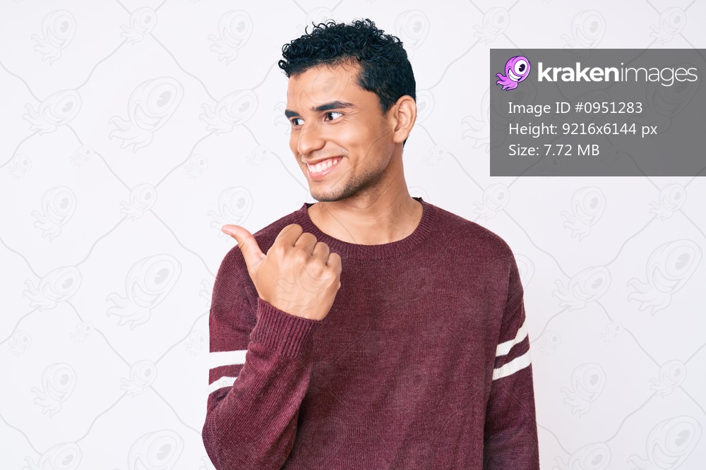 Young handsome hispanic man over white background pointing thumb up to the side smiling happy with open mouth 