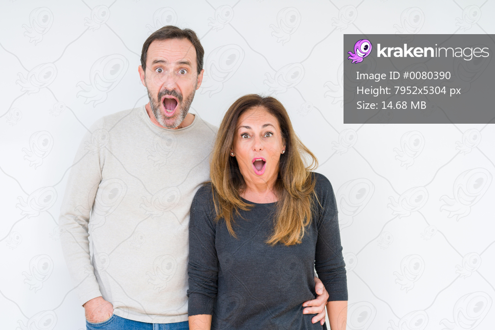 Beautiful middle age couple in love over isolated background afraid and shocked with surprise expression, fear and excited face.