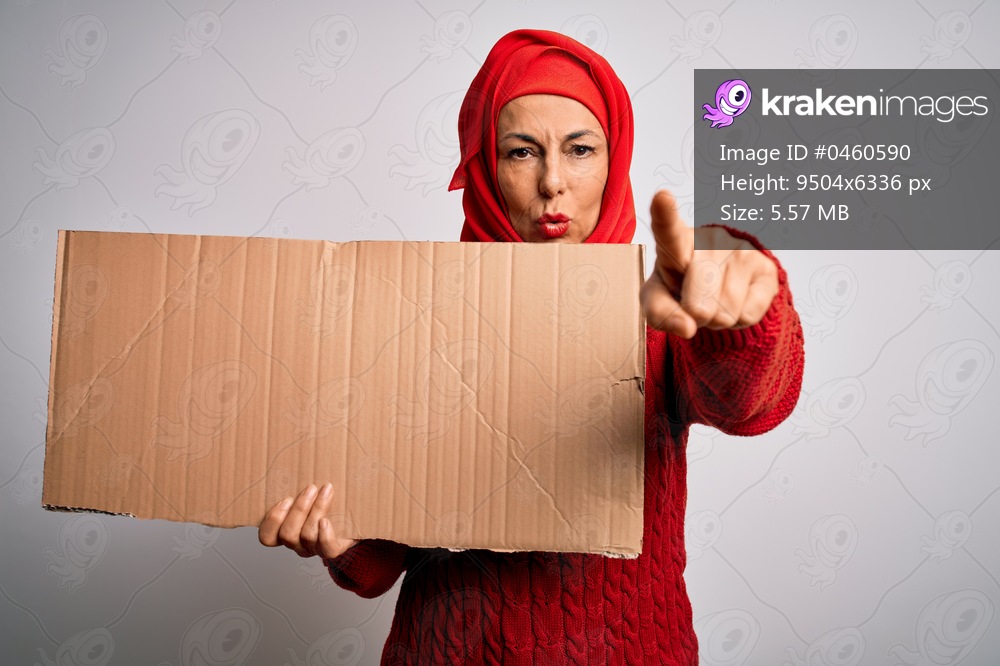 Middle age brunette woman wearing traditional muslim hijab holding banner pointing with finger to the camera and to you, hand sign, positive and confident gesture from the front