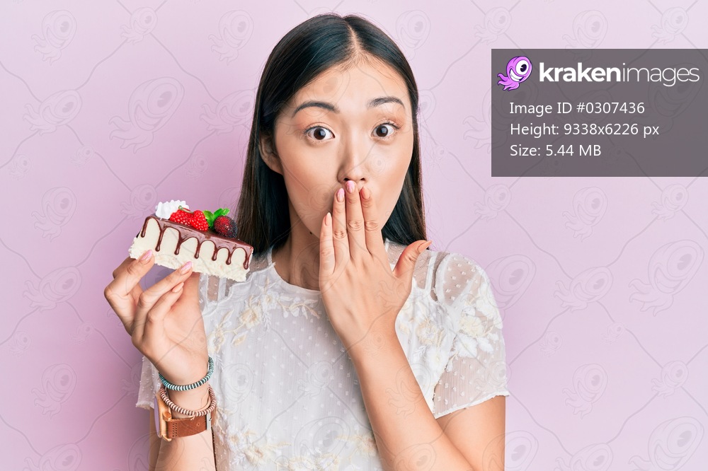 Young chinese woman eating a tasty cake covering mouth with hand, shocked and afraid for mistake. surprised expression 