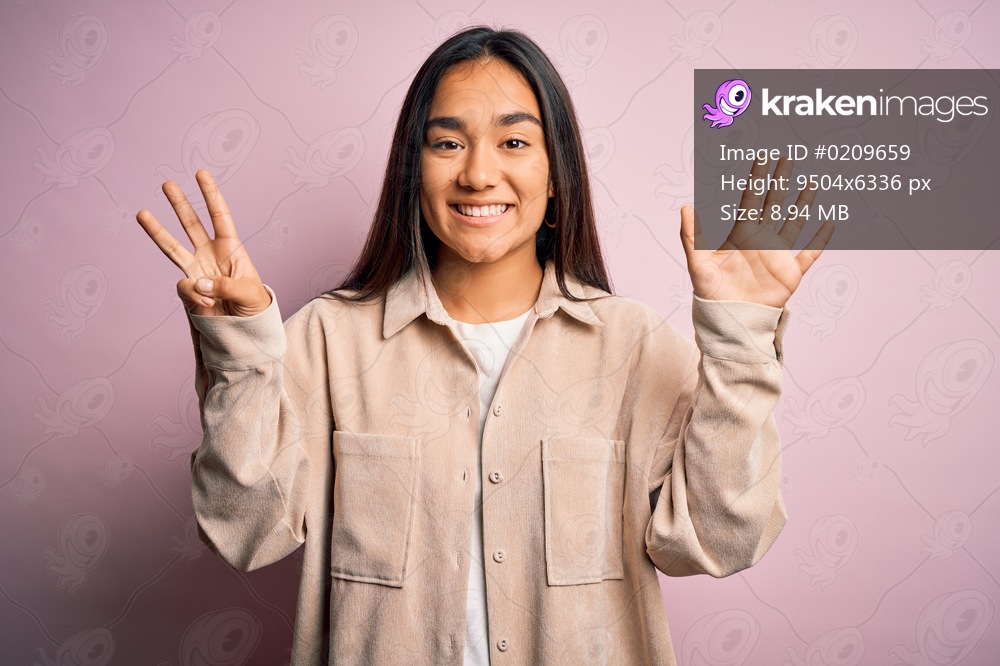 Young beautiful asian woman wearing casual shirt standing over pink background showing and pointing up with fingers number eight while smiling confident and happy.