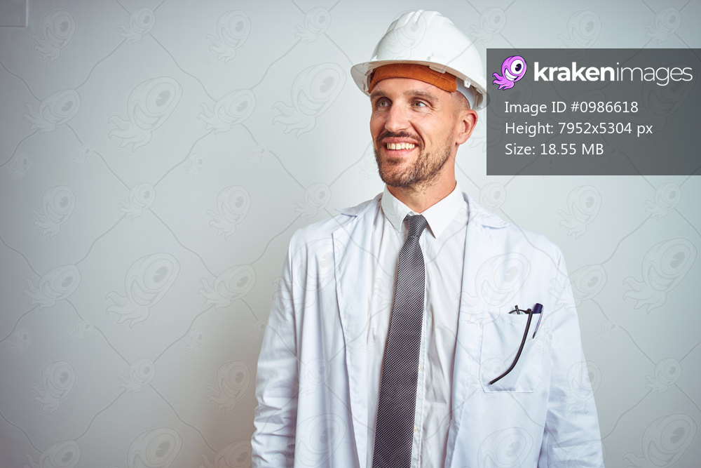 Young handsome engineer man wearing safety helmet over isolated background looking away to side with smile on face, natural expression. Laughing confident.