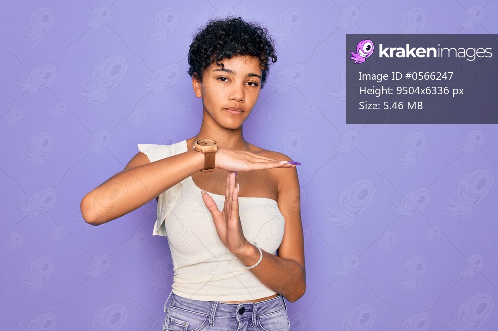 Young beautiful african american afro woman wearing casual t-shirt over purple background Doing time out gesture with hands, frustrated and serious face