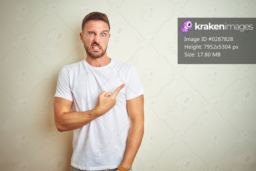 Young handsome man wearing casual white t-shirt over isolated background Pointing aside worried and nervous with forefinger, concerned and surprised expression