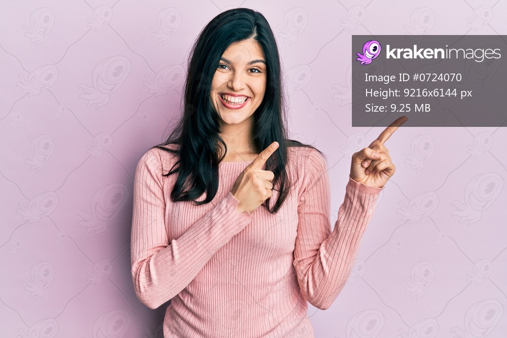 Young hispanic woman wearing casual clothes smiling and looking at the camera pointing with two hands and fingers to the side. 