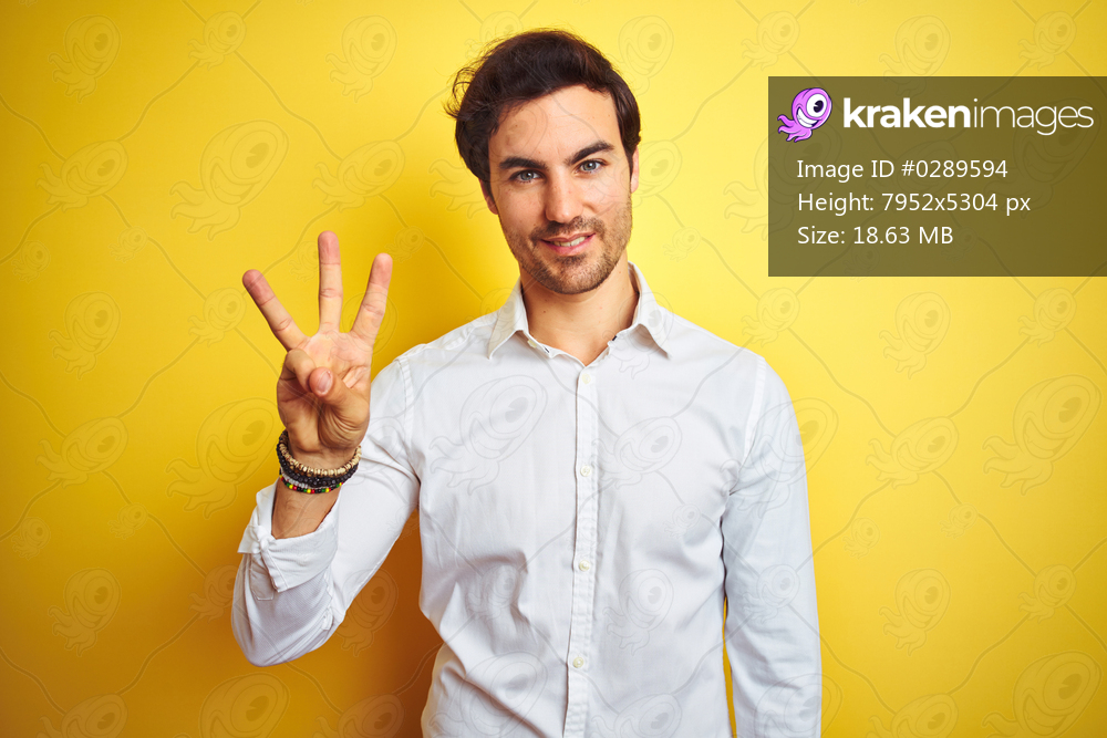 Young handsome businessman wearing elegant shirt standing over isolated yellow background showing and pointing up with fingers number three while smiling confident and happy.