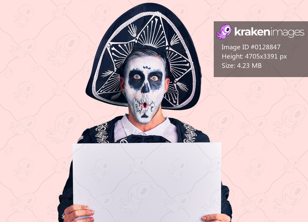 Young man wearing day of the dead costume holding blank empty banner scared and amazed with open mouth for surprise, disbelief face 