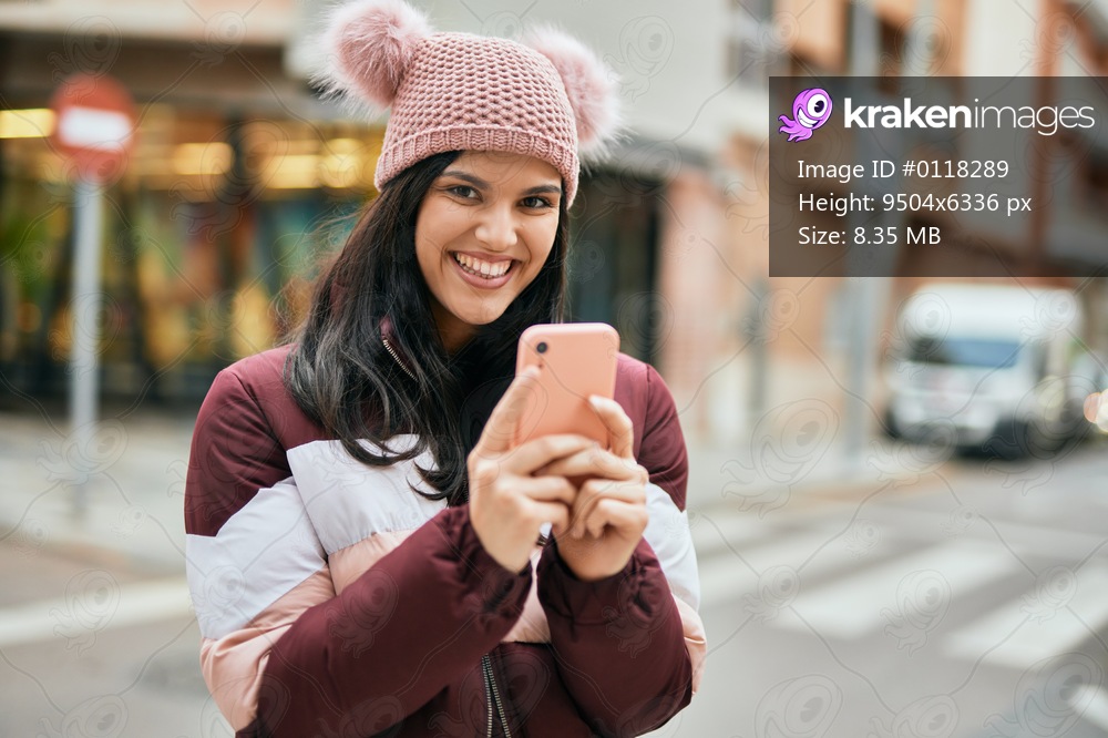 Young hispanic girl smiling happy using smartphone at the city.