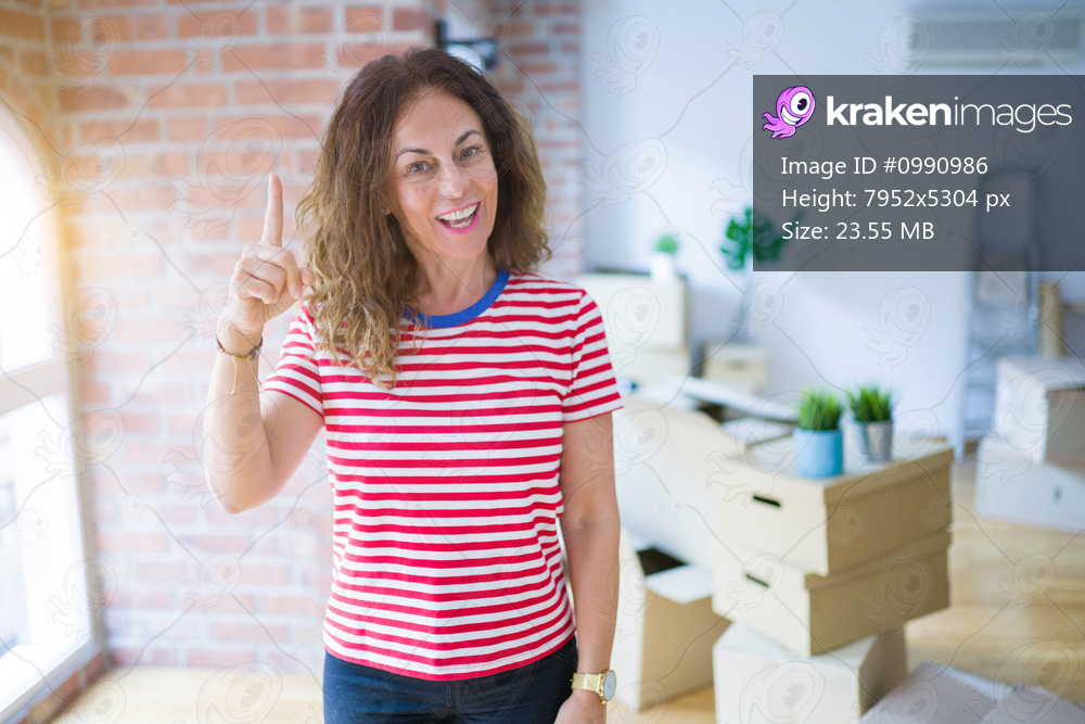 Middle age senior woman moving to a new house packing cardboard boxes pointing finger up with successful idea. Exited and happy. Number one.
