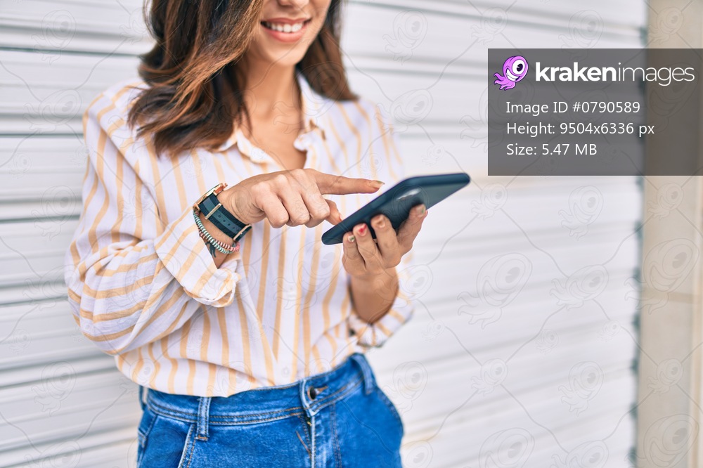 Young hispanic woman smiling happy using smartphone at the city.