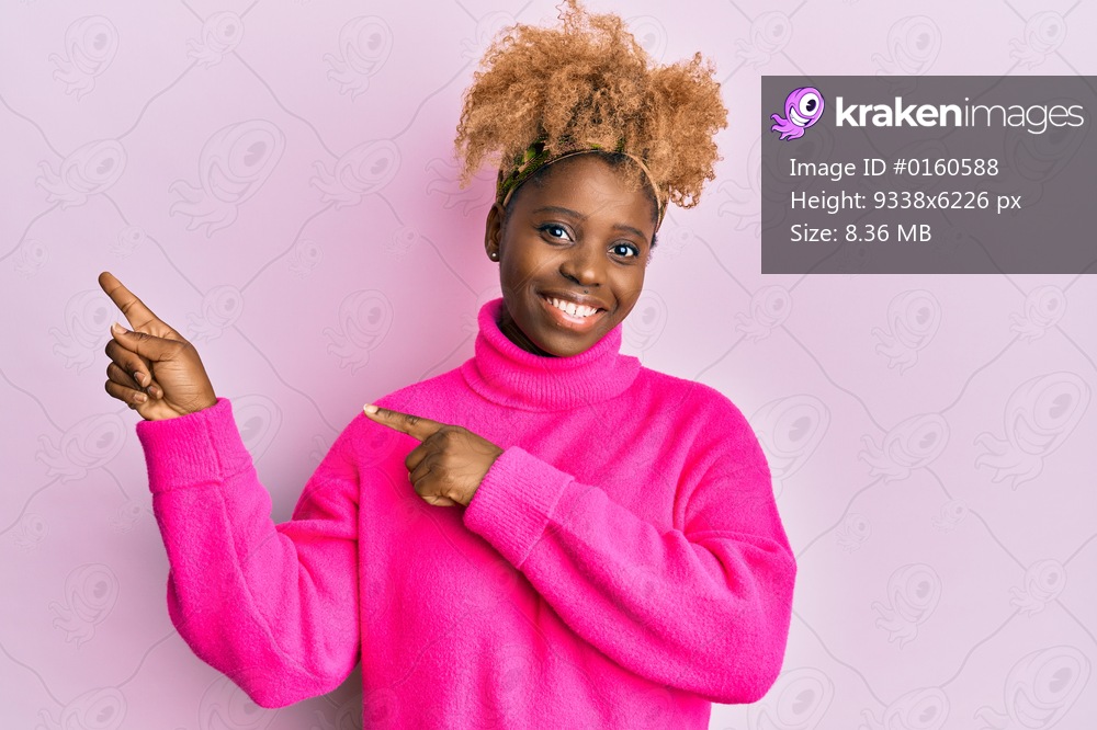 Young african woman with afro hair wearing casual winter sweater smiling and looking at the camera pointing with two hands and fingers to the side. 