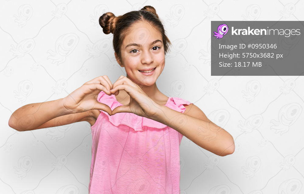 Beautiful brunette little girl wearing summer pink shirt smiling in love showing heart symbol and shape with hands. romantic concept. 
