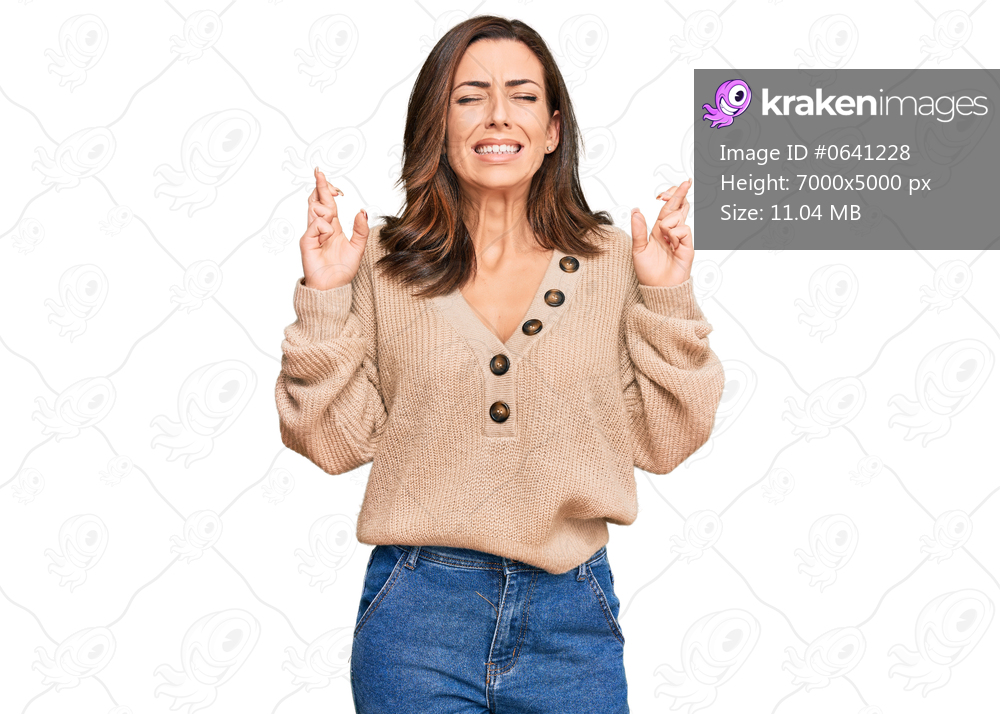 Young brunette woman wearing casual winter sweater gesturing finger crossed smiling with hope and eyes closed. luck and superstitious concept. 