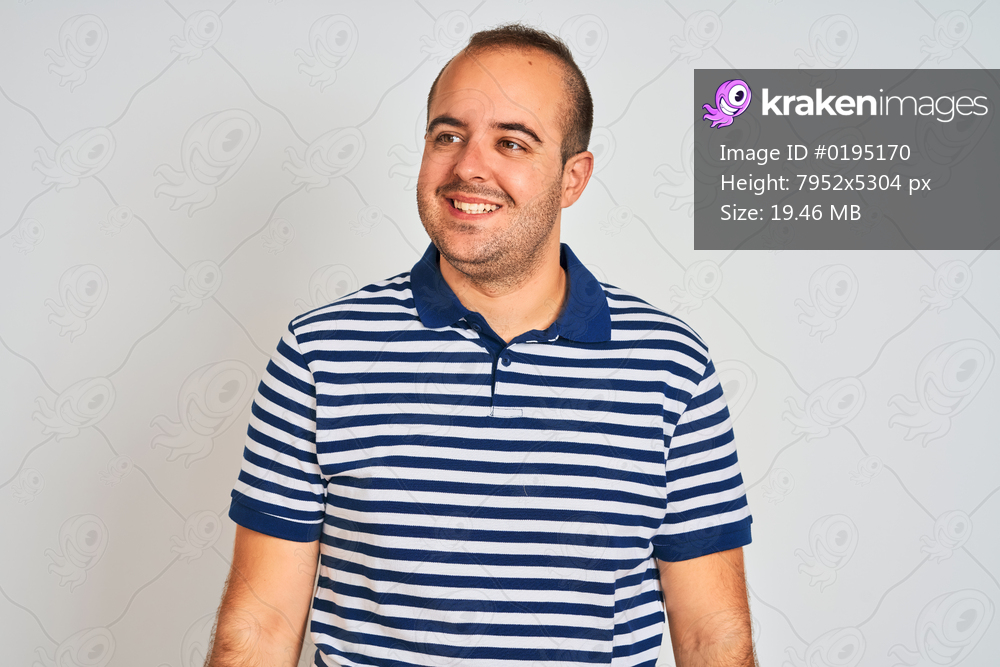 Young man wearing casual striped polo standing over isolated white background looking away to side with smile on face, natural expression. Laughing confident.