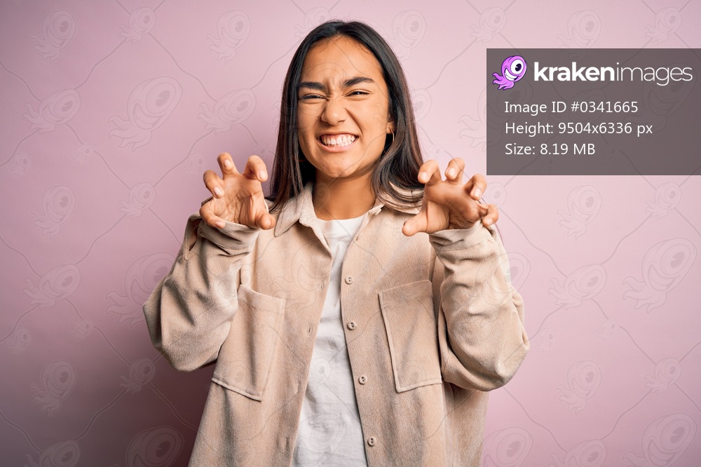 Young beautiful asian woman wearing casual shirt standing over pink background smiling funny doing claw gesture as cat, aggressive and sexy expression