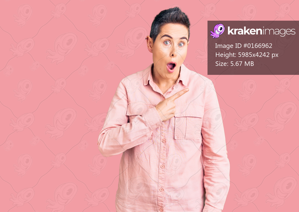 Young woman with short hair wearing casual clothes surprised pointing with finger to the side, open mouth amazed expression. 