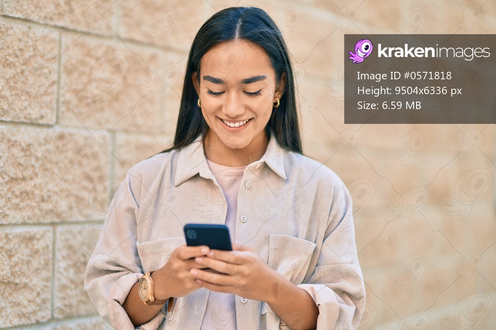 Young latin girl smiling happy using smartphone at the city.