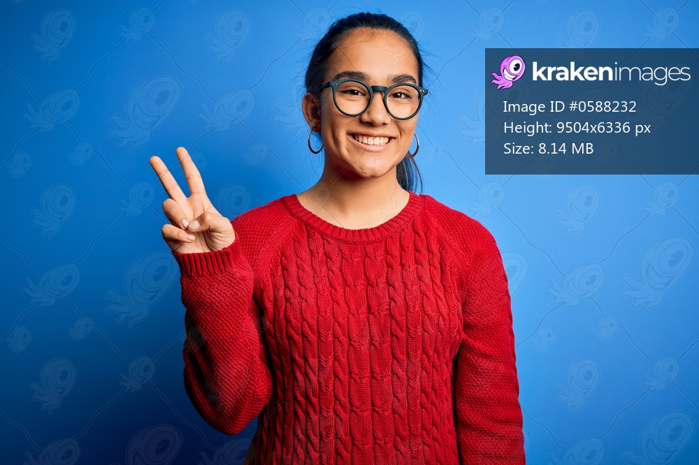 Young beautiful asian woman wearing casual sweater and glasses over blue background showing and pointing up with fingers number two while smiling confident and happy.