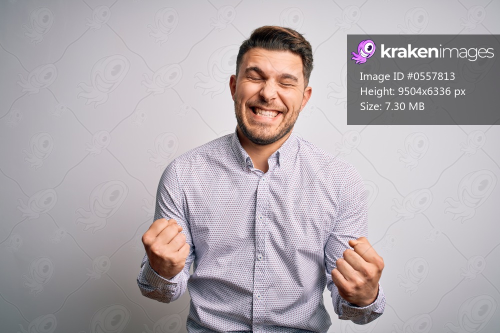 Young business man with blue eyes standing over isolated background very happy and excited doing winner gesture with arms raised, smiling and screaming for success. Celebration concept.