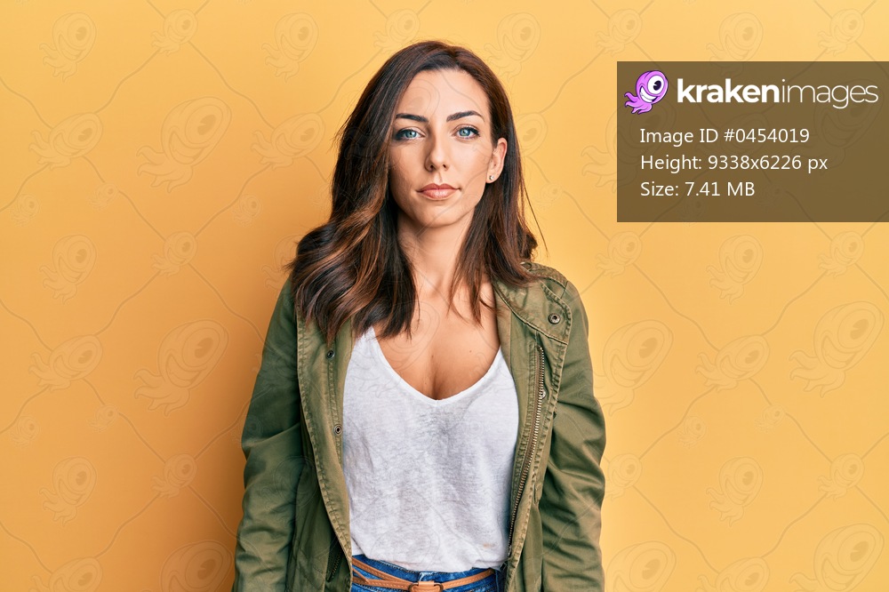 Young brunette woman wearing casual clothes over yellow background with serious expression on face. simple and natural looking at the camera. 