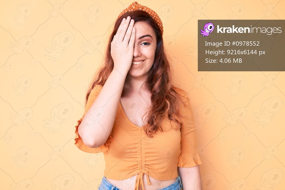 Young beautiful woman wearing casual clothes covering one eye with hand, confident smile on face and surprise emotion. 