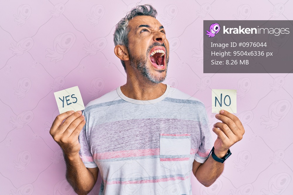Middle age grey-haired man holding yes and no reminder angry and mad screaming frustrated and furious, shouting with anger looking up. 