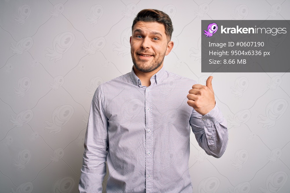 Young business man with blue eyes standing over isolated background smiling with happy face looking and pointing to the side with thumb up.