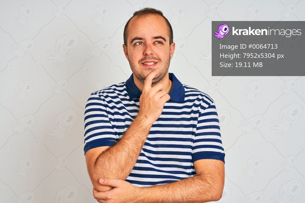 Young man wearing casual striped polo standing over isolated white background with hand on chin thinking about question, pensive expression. Smiling and thoughtful face. Doubt concept.